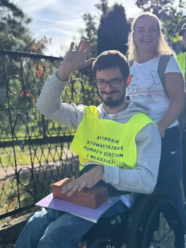 Uczestnik sztafety w żółtej kamizelce z nazwą Bytomskiego Stowarzyszenia Pomocy Dzieciom i Młodzieży Niepełnosprawnej.
