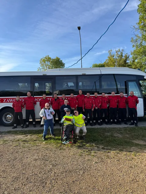 Uczestnicy sztafety w żółtych kamizelkach ze strażakami przy autobusie.
