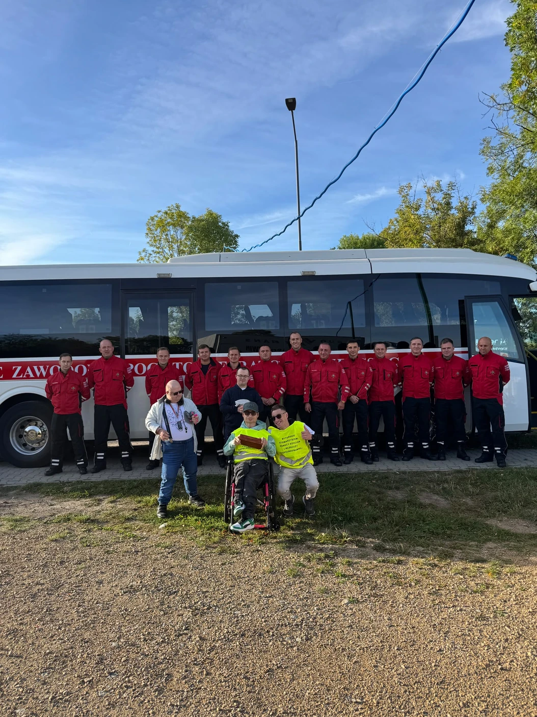 Uczestnicy sztafety w żółtych kamizelkach ze strażakami przy autobusie.