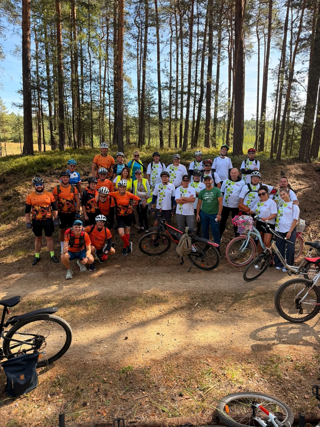 Grupa rowerzystów wspierających sztafetę na leśnej drodze.
