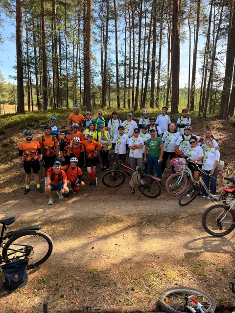 Grupa rowerzystów wspierających sztafetę na leśnej drodze.